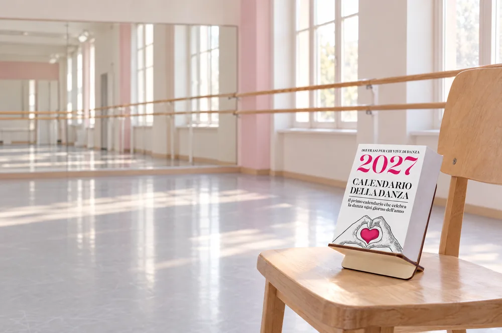 Il Calendario della Danza 2027 su una sedia di legno in una grande sala danza luminosa, con le sbarre e gli specchi